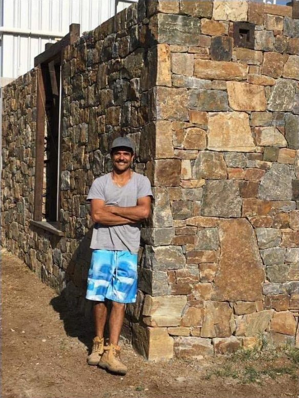 Aldo Mclaren, owner and stonemason, beside a stone wall he built